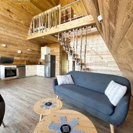 Vue sur le salon cosy et la cuisine moderne du chalet Charkhan en Aframe, à 10 km de Gérardmer, avec une mezzanine en bois naturel.