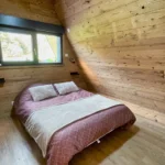 Chambre du chalet Charkhan en Aframe à 10 km de Gérardmer, équipée d'un lit double et d'un lit bébé, avec des finitions en bois naturel.