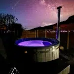 Bain nordique illuminé de nuit sous un ciel étoilé dans les Vosges aux Atypiques Chalets