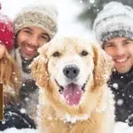 Famille souriante jouant dans la neige avec un chien devant un chalet à Gérardmer.
