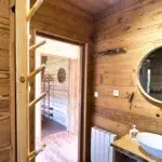 Salle de bain en bois du chalet Aslan avec vasque blanche et miroir rond