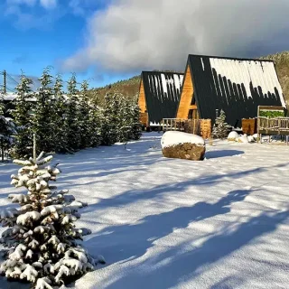 Les 3 chalets atypiques sous la neige - Les Atypiques Chalets Vosges Vue hivernale des trois chalets A-frame des Atypiques Chalets dans les Vosges, sapins enneigés et ciel bleu