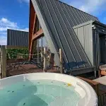 Bain nordique rond en extérieur devant le chalet A-Frame Iorik, terrasse en bois et ciel bleu, près de Gérardmer dans les Vosges