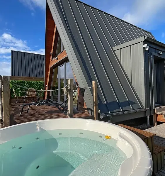 Bain nordique rond en extérieur devant le chalet A-Frame Iorik, terrasse en bois et ciel bleu, près de Gérardmer dans les Vosges