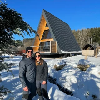 Chalet Charkhan im Winter unter Schnee Paar vor dem verschneiten A-Frame-Chalet Charkhan, blauer Winterhimmel in den Vogesen bei Gérardmer